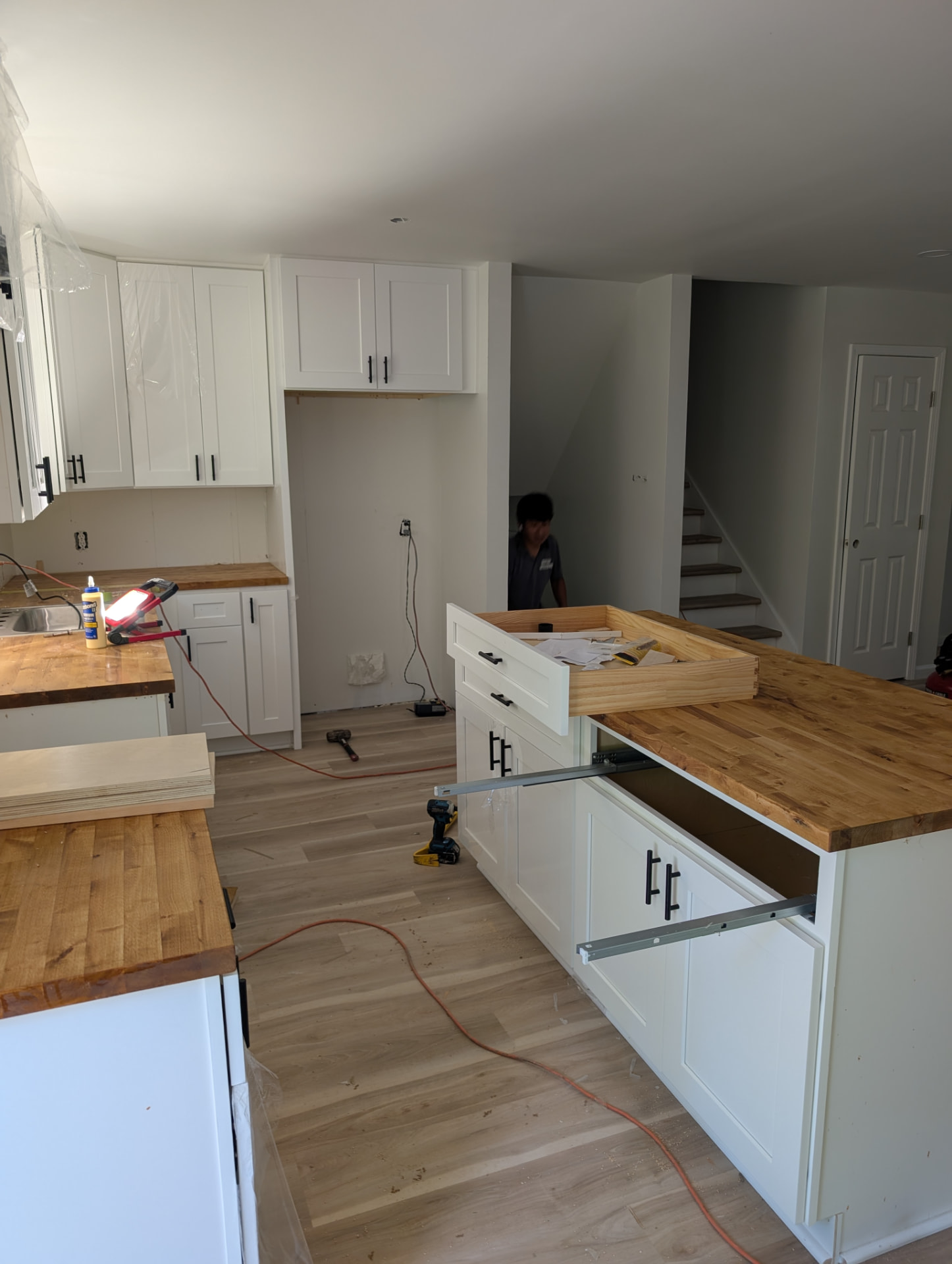 Kitchen island under construction with drawer boxes and butcher block top, stairs visible behind