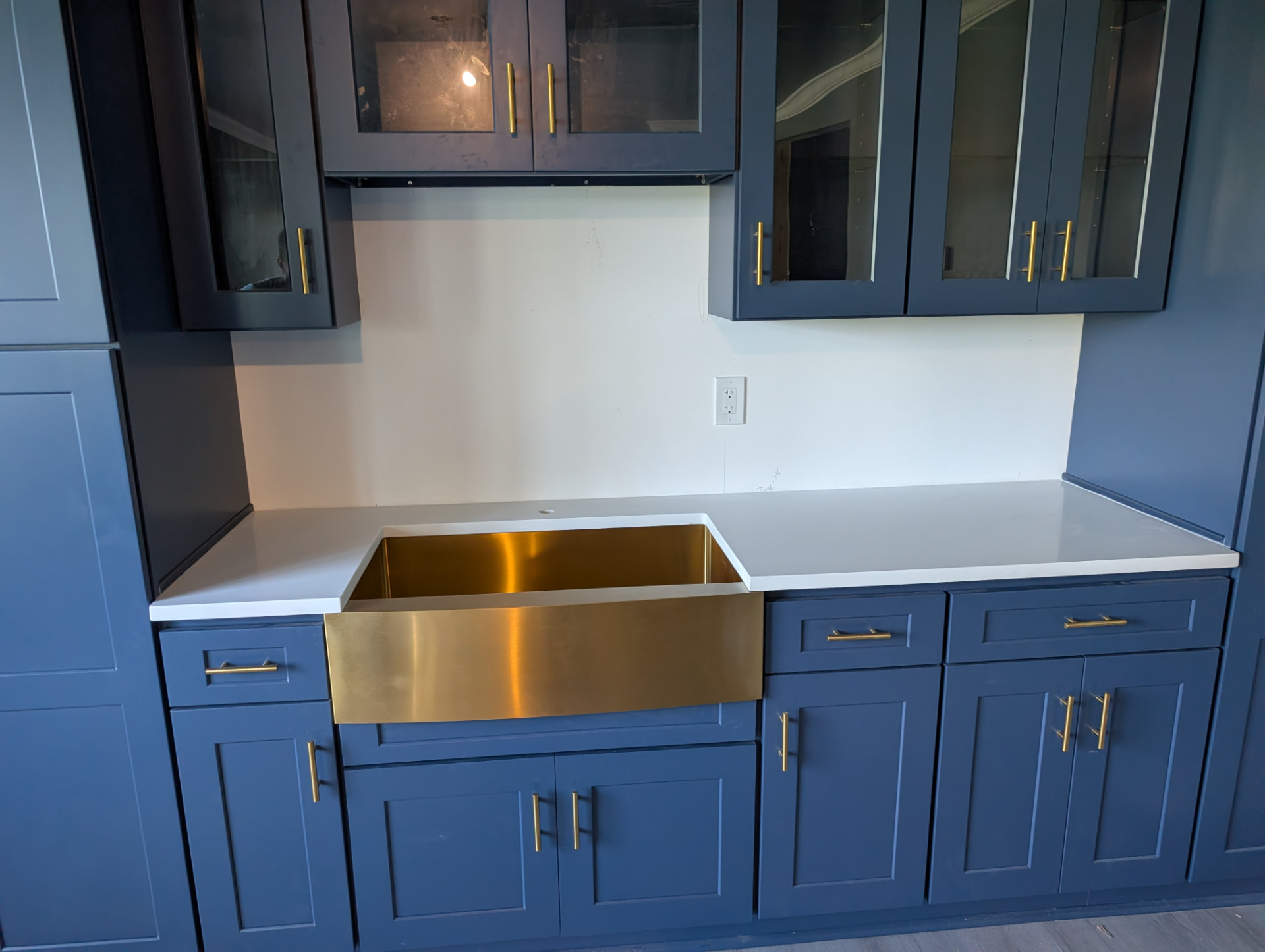 White quartz counter with brushed brass farmhouse apron sink set into navy blue shaker cabinets