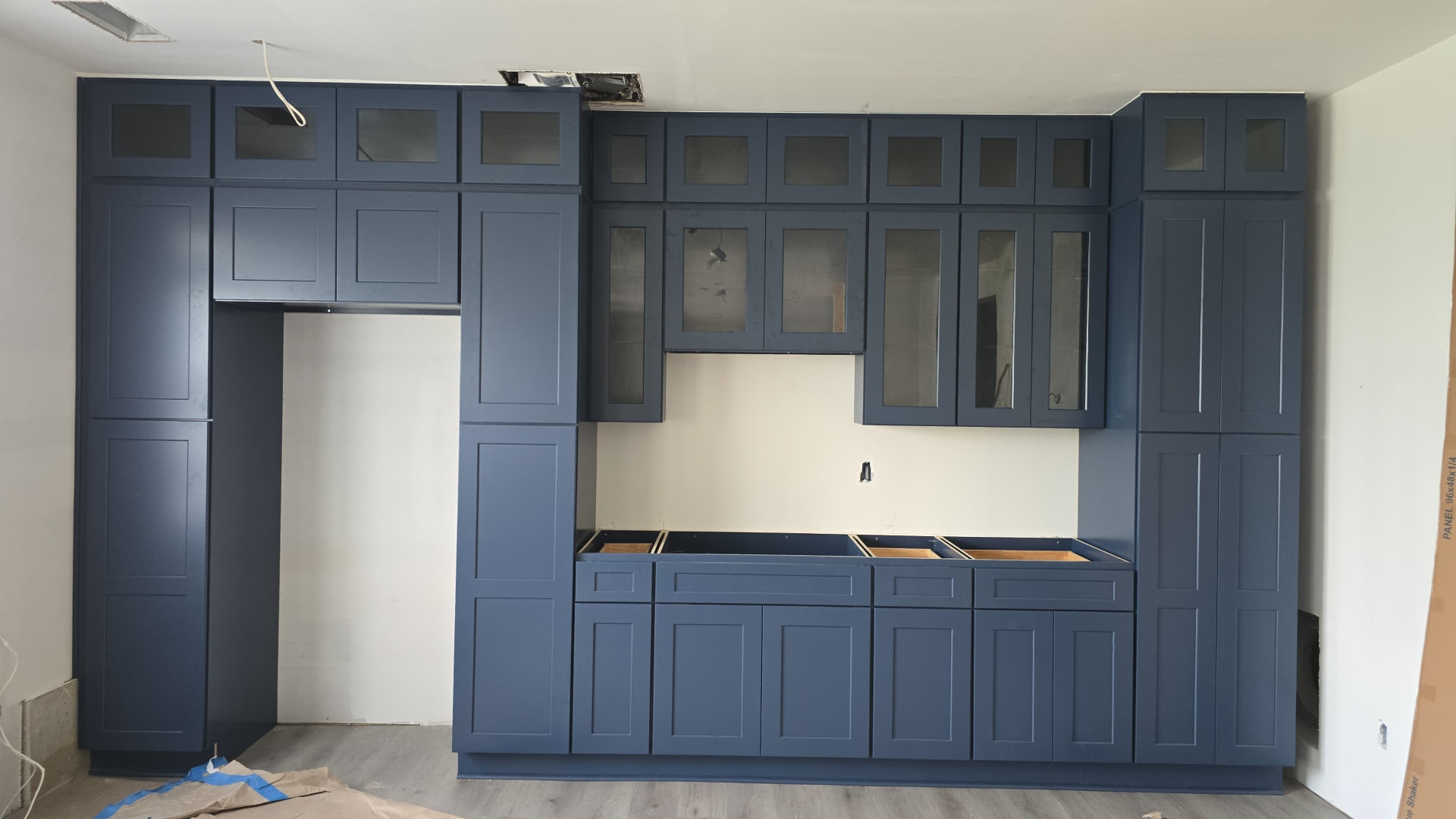 Navy blue shaker kitchen cabinet wall with stacked glass-front uppers, installed floor to ceiling