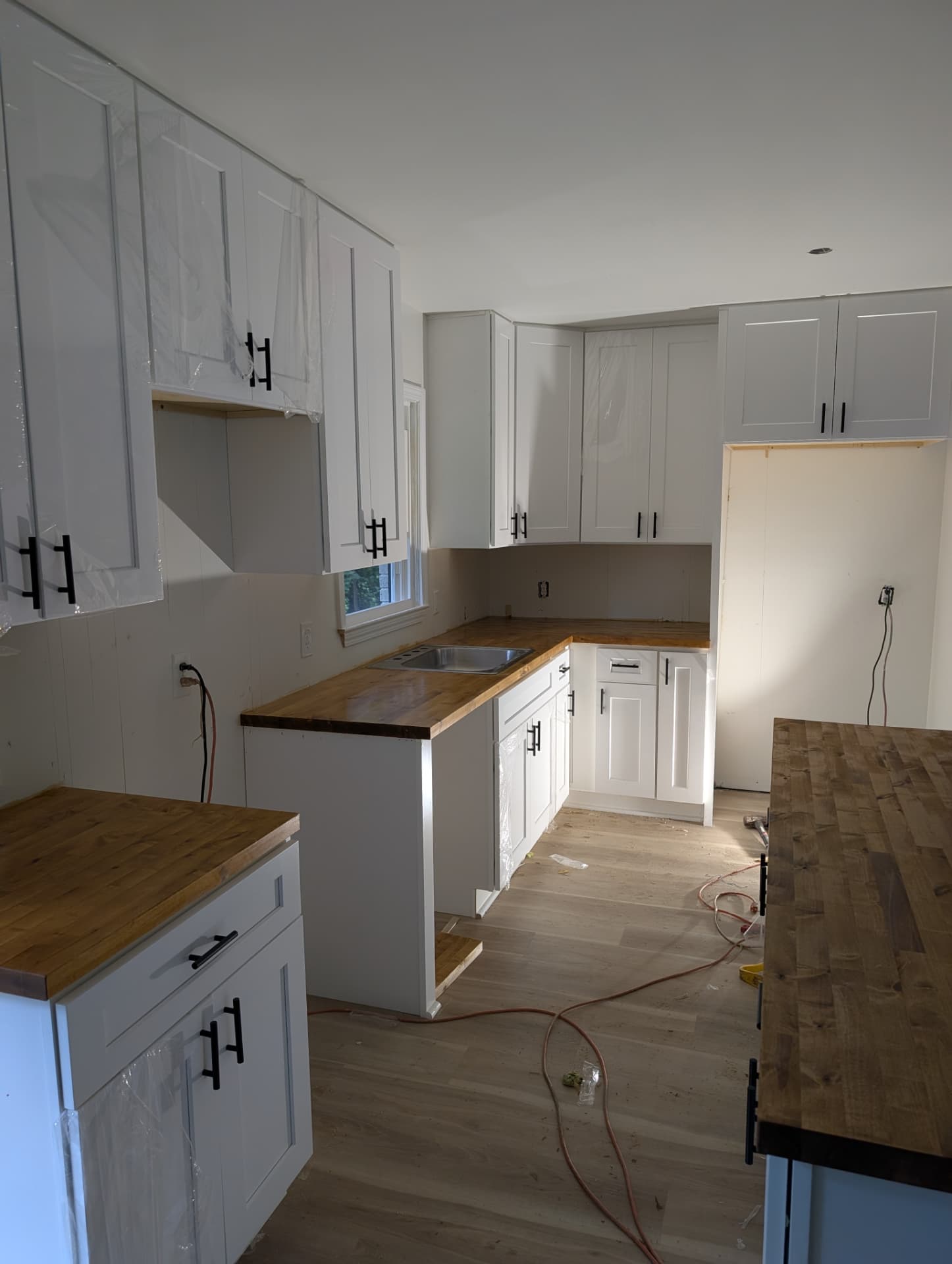 Finished painted shaker kitchen with butcher block counters, stainless sink under the window and tall cabinet run